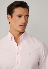 Light pink button-up shirt made from cotton, featuring a small blue logo on the chest and a classic collar design.