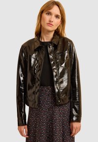 Chaqueta de cuero sintético negra con un diseño corto, cierre de botones y bolsillos en el pecho, combinada con una falda de estampado floral.