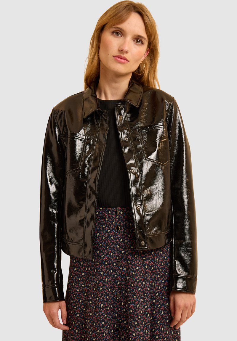 Chaqueta de cuero sintético negra con un diseño corto, cierre de botones y bolsillos en el pecho, combinada con una falda de estampado floral.