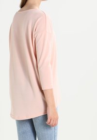 Helles rosa Langarmoberteil mit U-Boot-Ausschnitt, weichem Material und entspannter Passform, kombiniert mit blauen Jeans.