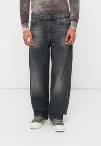 Χαλαρά, σκουρόχρωμα γκρι τζιν με ξεθωριασμένο φινίρισμα, διακριτική φθορά και σχέδιο με πέντε τσέπες. Συνδυασμένα με γκρι αθλητικά παπούτσια.