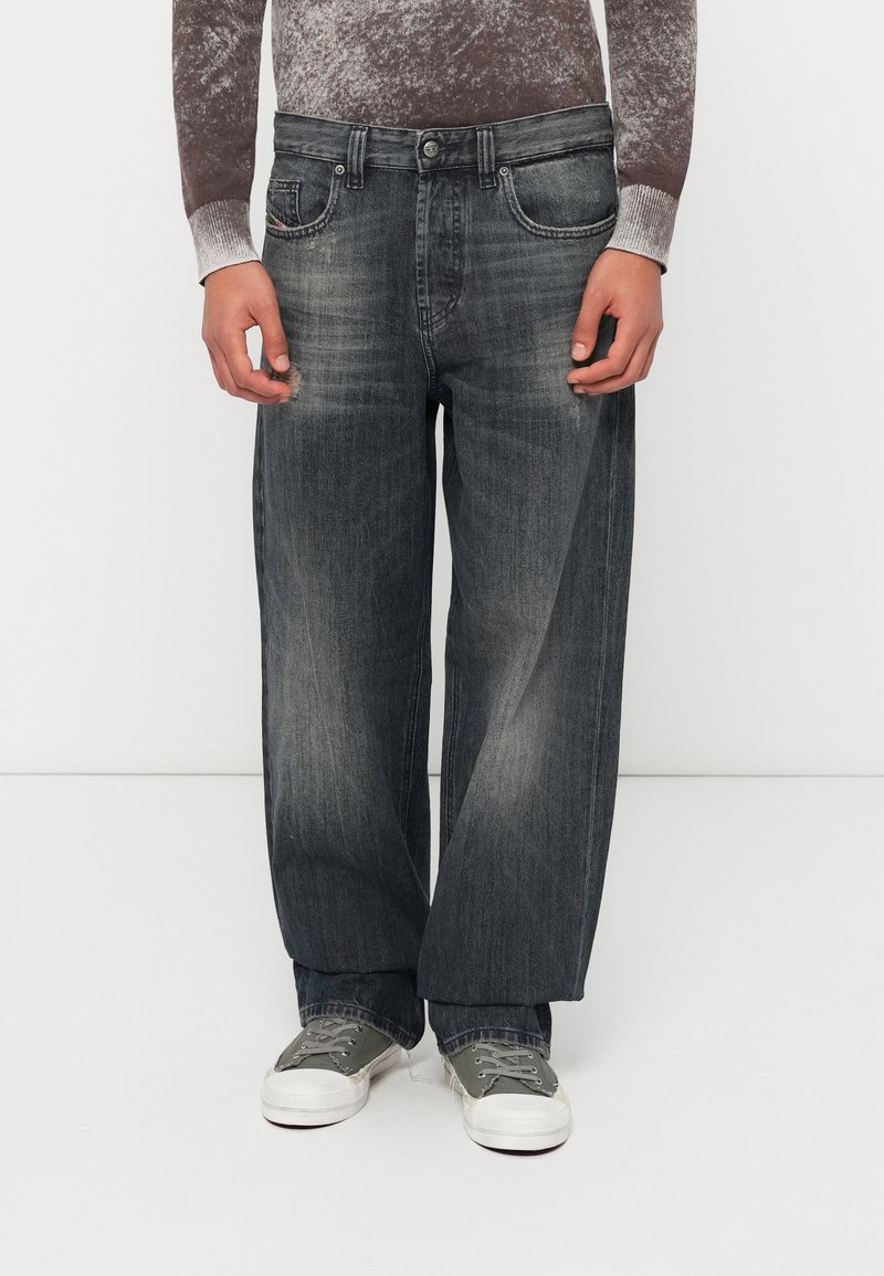 Χαλαρά, σκουρόχρωμα γκρι τζιν με ξεθωριασμένο φινίρισμα, διακριτική φθορά και σχέδιο με πέντε τσέπες. Συνδυασμένα με γκρι αθλητικά παπούτσια.