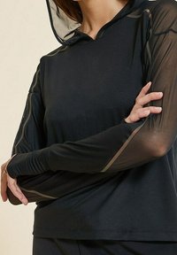 Black hooded top with sheer mesh long sleeves, featuring a fitted design and subtle sheen. Smooth texture with a layered appearance.