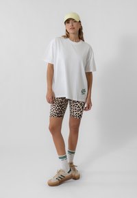 Valge ülikerge t-särk rohelise tekstiga, millele on sobitatud leopardimustrilised rattapüksid. Beežid spordijalatsid roheliste triipudega, valged sokid roheliste aktsentidega.