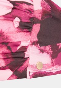 Top da bagno con stampa astratta rosa e bordeaux, texture a pieghe e un accento logo in tono oro vicino alla cucitura. Materiale morbido e elastico.