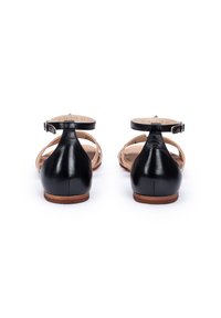 Zwarte leren sandalen met een enkelbandje, platte zolen en een gesloten hiel. Het ontwerp bevat kruislijnen en een natuurlijk gekleurde binnenzool.