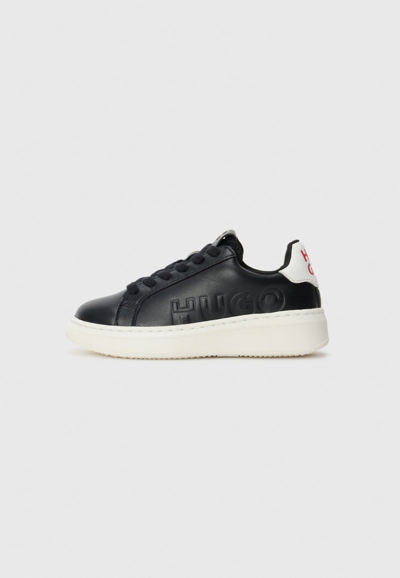Baskets en cuir noir avec le mot "HUGO" en relief sur le côté, semelle blanche, lacets noirs et languette blanche au talon avec le lettrage rouge "HUGO".