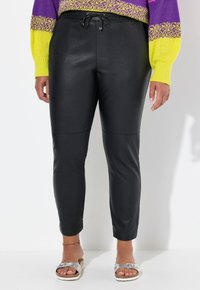 Joggers neri in finta pelle con un design aderente, vita con cordoncino e caviglie affusolate. Texture liscia con dettagli di cucitura discreti.
