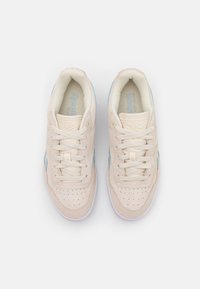 Pár béžových semišových tenisek Reebok s světle modrými akcenty, bílou podrážkou a tkaničkami, z pohledu shora na jednoduchém bílém pozadí.