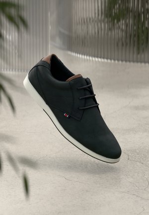 Czarny skórzany but z brązowymi akcentami, zaokrąglonym noskiem i białą podeszwą. Posiada sznurowanie oraz mały trójkolorowy detal z boku.