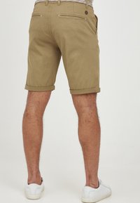 Pantaloni scurți khaki cu manșete răsucite, având buzunare pe spate și o textură netedă dintr-un amestec de bumbac. Asociati cu adidași albi.