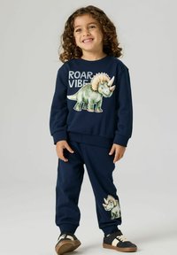 Set composto da felpa e pantaloni blu navy con grafica di un dinosauro, testo "ROAR VIBE", dettagli ricamati e polsini elasticizzati per il massimo comfort.