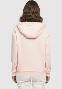 Felpa rosa con cappuccio, vestibilità rilassata, tessuto morbido, polsini e orlo a costine, e una grande tasca sul retro. Presenta un cappuccio con cordino.