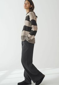 Stribet hættetrøje i beige og sort, med en kort, løs pasform og ribbede mansjetter. Sammen med løse mørkegrå bukser og sorte slip-on sko.