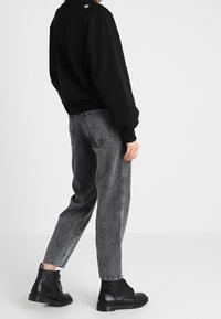 Felpa nera con scollo tondo, jeans grigi a vita alta con finitura sbiadita e stivaletti neri con lacci.