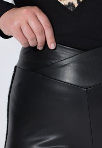 Zwarte faux leren broek met een brede, contourede tailleband en een strakke, gladde textuur; met een decoratieve zwarte kraalaccent aan de zijkant.