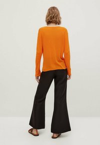 Oranger, gerippter Pullover mit langen Ärmeln, kombiniert mit schwarzen, weit geschnittenen Hosen. Die Textur ist weich und die Passform entspannt.