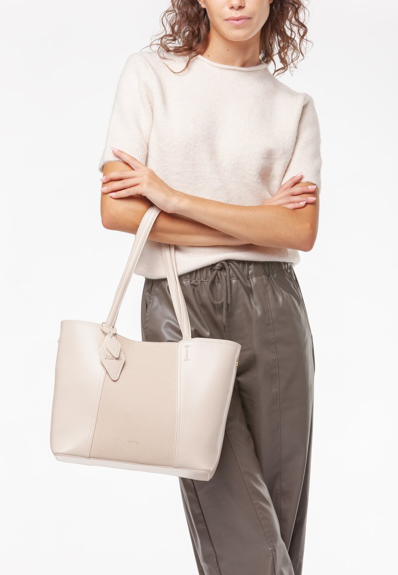 Borsa a tote in pelle beige con un pannello testurizzato, dotata di doppi manici e un tag decorativo. Materiale morbido e liscio con una forma strutturata.