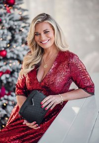 Red sequin dress with a V-neckline, paired with a black quilted handbag. Long, wavy blonde hair, with a gold necklace and bracelet.