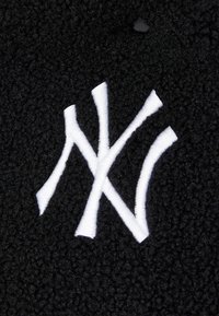 Μαύρος φλις ύφασμα με μαλακή υφή διαθέτει το λογότυπο NY σε λευκό κεντητό σχέδιο. Ο σχεδιασμός περιλαμβάνει λεπτομέρεια στρογγυλού κουμπιού.