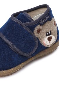 Niebieskie filcowe kapcie z paskiem na rzep. Na boku naszyty jest wizerunek misia z haftowanymi detalami. Teksturowana gumowa podeszwa zapewniająca przyczepność.