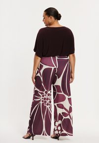 Locker sitzendes, kastanienbraunes Oberteil kombiniert mit weit geschnittenen Hosen mit großem Blumenmuster in Burgund- und Cremetönen, glatter Stoff, weicher Fall.