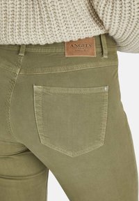 Jeans de denim verde oliva que cuentan con un bolsillo trasero con detalles de costura y una etiqueta marrón en la cinturilla que dice "ANGELS". Tejido texturizado.