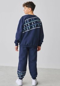 Marineblaues Sweatshirt- und Hosenset aus weichem Stoff, mit weißen und türkisfarbenen horizontalen Textmustern auf der Rückseite und an den Bündchen.