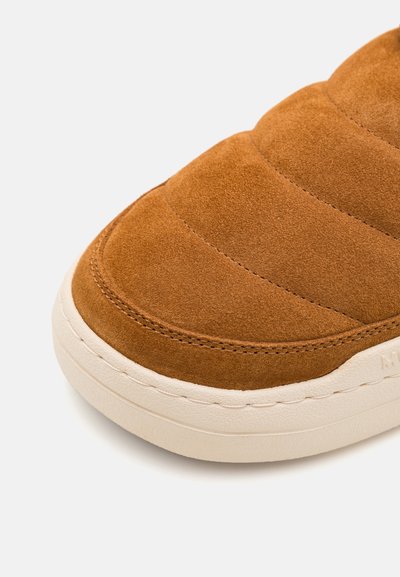 Brązowy zamszowy but typu slip-on z pikowanym wzorem, okrągłym noskiem i kremową gumową podeszwą z widocznymi detalami przeszycia.