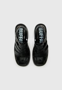 Black sandal with woven design, adjustable strap, textured upper, and flat sole. Inside features a large logo on a light background.