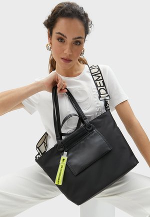 Bolsa tote negra hecha de un material elegante, con asas dobles, un bolsillo con cremalleras en la parte frontal y una etiqueta de color verde brillante. Correa de contraste con detalle de logo.