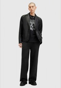 Svart läderblazer över en grafisk svart t-shirt, kombinerad med vida svarta och vita randiga byxor. Svarta skor fulländar outfiten.
