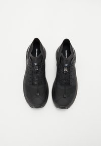 Baskets de sport noires avec une tige en synthétique, des panneaux en maille texturée, un système de laçage rapide et une semelle rembourrée pour le confort et le soutien.