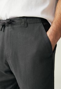 Pantalons en lin noir mélangé avec une coupe décontractée, dotés d'une taille avec cordon de serrage ajustable et de poches latérales. Tissu texturé avec une finition mate.