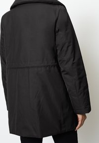 Cappotto isolato nero con un design elegante, caratterizzato da un colletto rialzato, maniche lunghe e una texture liscia. Cuciture visibili sulla parte posteriore.