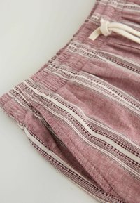 Gros plan sur un tissu rayé rose et blanc avec une taille élastique et un cordon blanc, probablement une partie d'un short ou d'un pantalon décontracté.