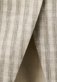 Tessuto in lino a righe beige e crema con trama strutturata, piegato per mostrare i dettagli del tessuto e le fibre naturali.