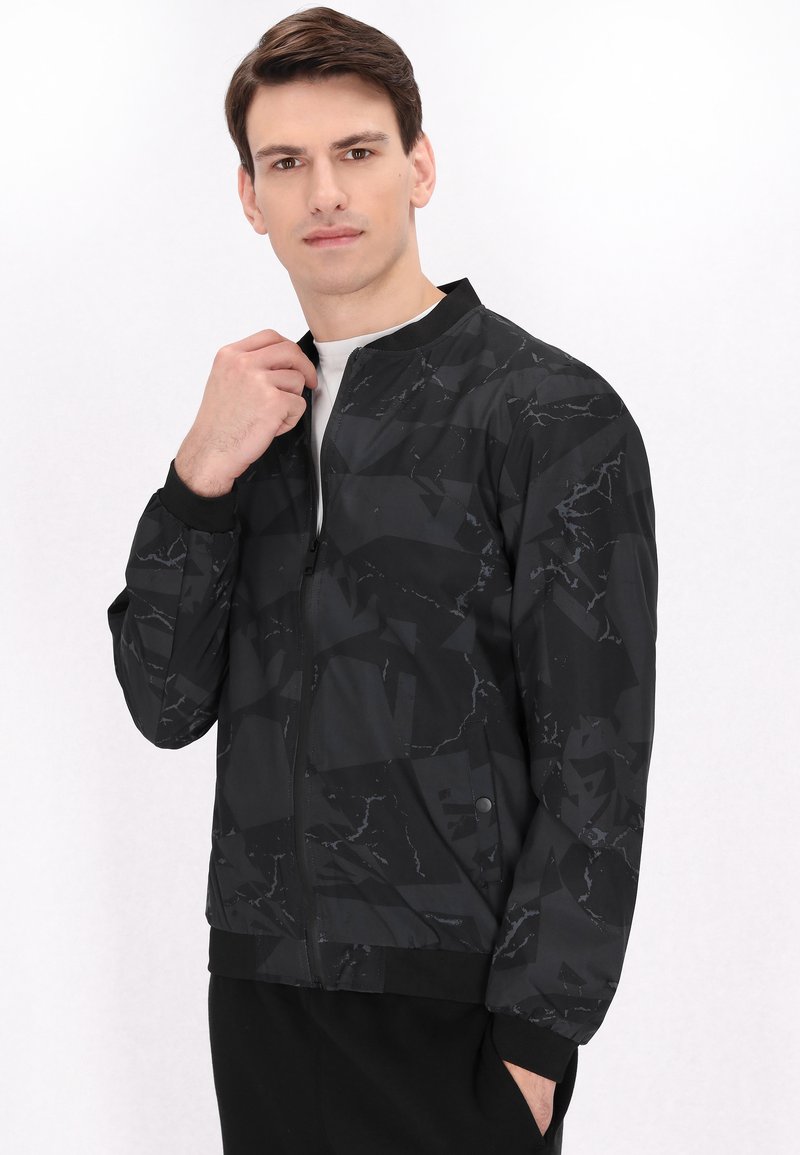 Giacca bomber nera con un motivo marmoreo geometrico, chiusura con zip, colletto e polsini a costine, realizzata in tessuto leggero e liscio.
