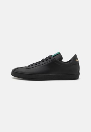 Adidași din piele neagră, cu vârf rotund, șireturi plate, accent verde pe limbă și siglă aurie pe toc. Talpă din cauciuc texturat.