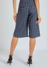 Culottes marinos con un patrón de cuadrícula. Hechas de una tela ligera, con una cintura alta, bolsillos y una longitud recortada, combinadas con tacones negros.