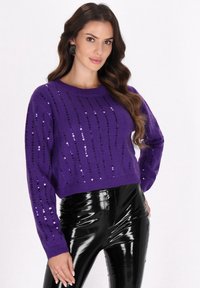 Pulover scurt tricotat de culoare mov cu paiete dispuse pe verticale, guler rotund și mâneci lungi, asortat cu pantaloni negri lucioși.