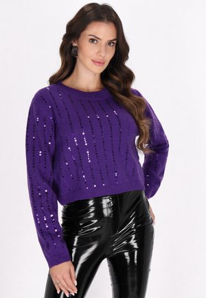 Maglione corto in maglia viola con paillettes disposte in righe verticali, colletto rotondo e maniche lunghe, abbinato a pantaloni neri lucidi.