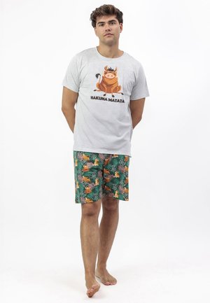 Joven descalzo que lleva una camiseta gris claro con la frase "Hakuna Matata" y un jabalí de dibujos animados, y pantalones cortos verdes con estampado de animales de la jungla.