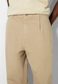 Beiga, plisserade byxor i slät tyg. Har en metallknappstängning och sidfickor. Standardpassform med rak bendesign.