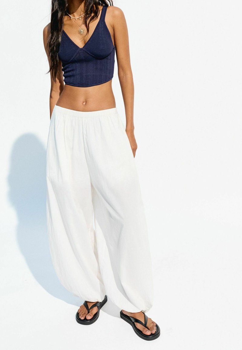 Haut court côtelé bleu marine, pantalon blanc ample et tongs noires. Les tissus semblent légers ; les modèles sont simples et décontractés.