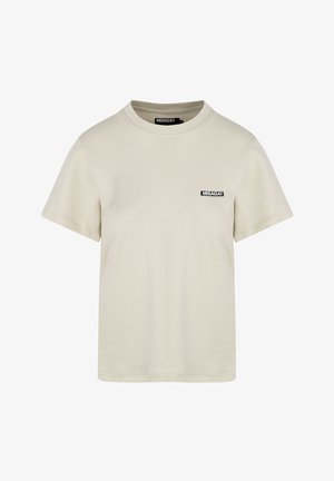 Beżowa bawełniana koszulka z okrągłym dekoltem i krótkimi rękawami. Na przodzie znajduje się mała czarna metka z logo. Gładka tekstura, standardowy krój.