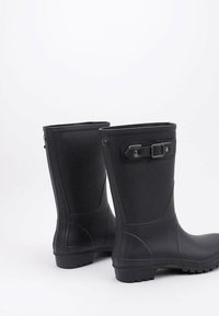Bottes de pluie en caoutchouc noir avec une finition mate lisse, à hauteur de cheville, dotées d'une boucle décorative et d'une semelle texturée pour une meilleure adhérence.