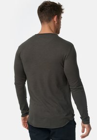Camisa de manga larga gris oscuro con escote redondeado y mangas ajustadas, hecha de un tejido suave, con un dobladillo trasero ligeramente más largo.