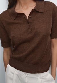 Brunic kortärmad polo skjorta gjord av texturerat stickat tyg, med krage och tre knappar, samt ribbad nederkant.