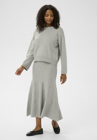 Pull en laine grise avec épaules tombantes associé à une jupe maxi grise ajustée avec un ourlet évasé et un tissu texturé. Chaussures plates noires.